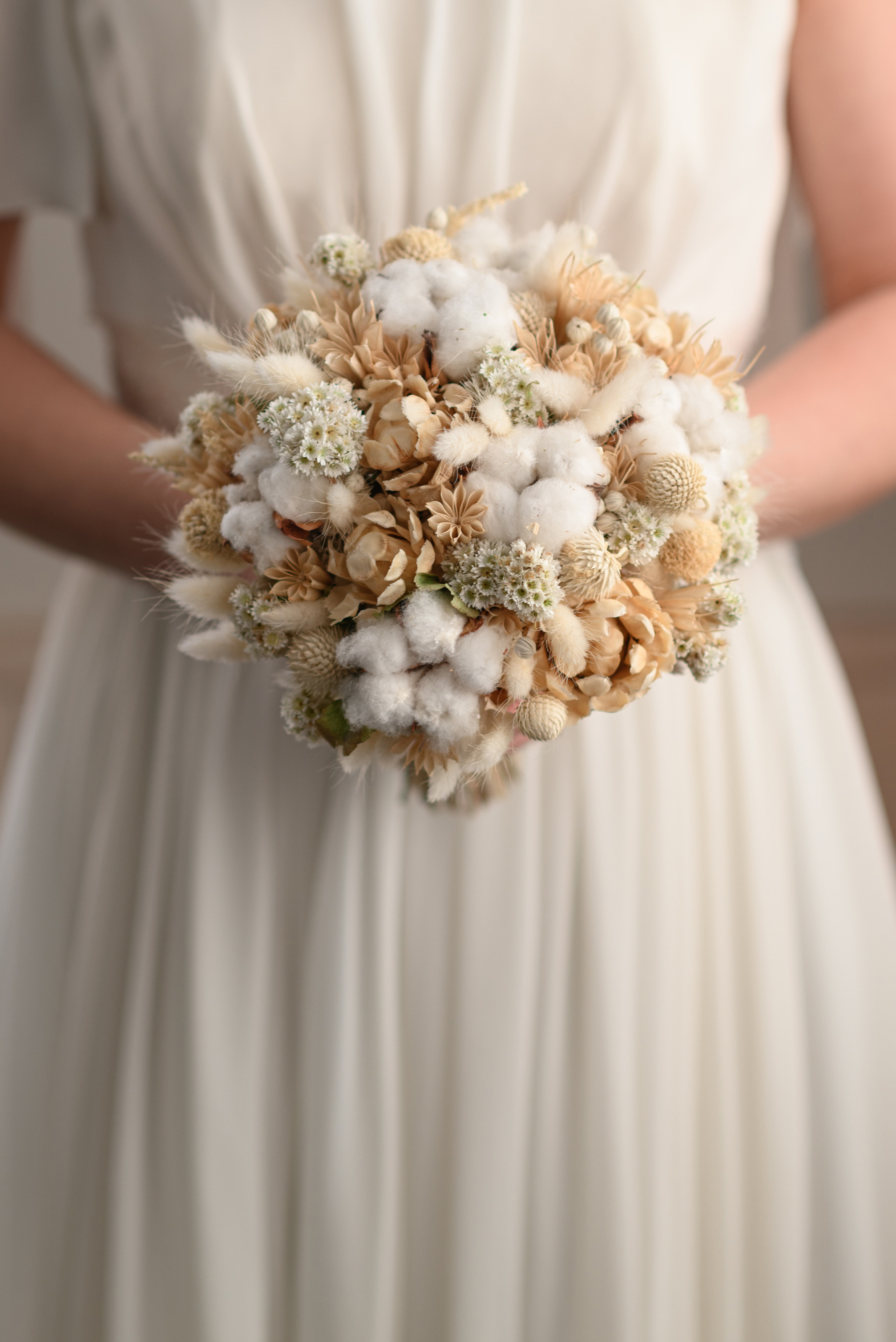 Light-coloured dried flower bridal bouquet held in front of a dress