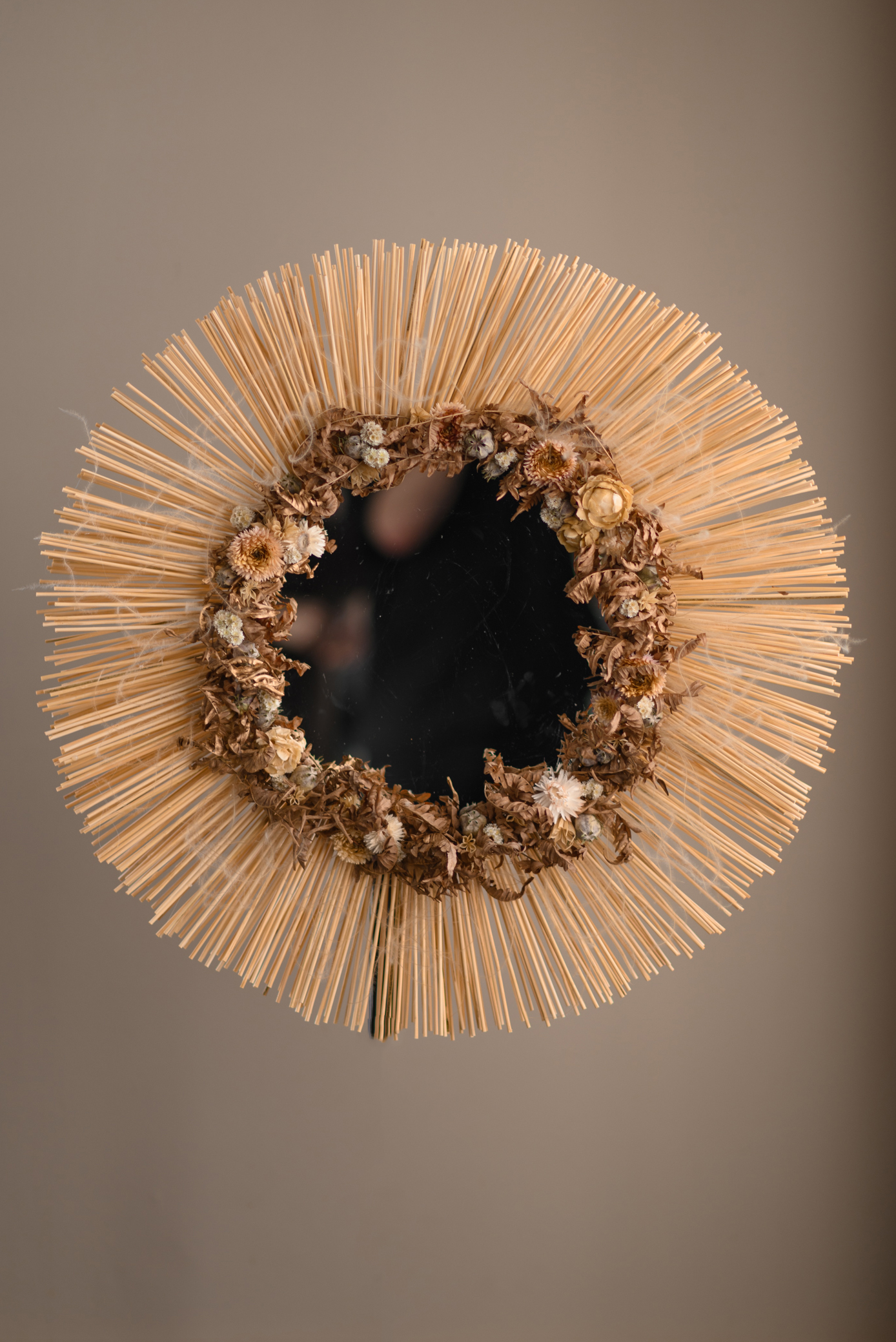 Round mirror with a dried flower border and radiating pale stems