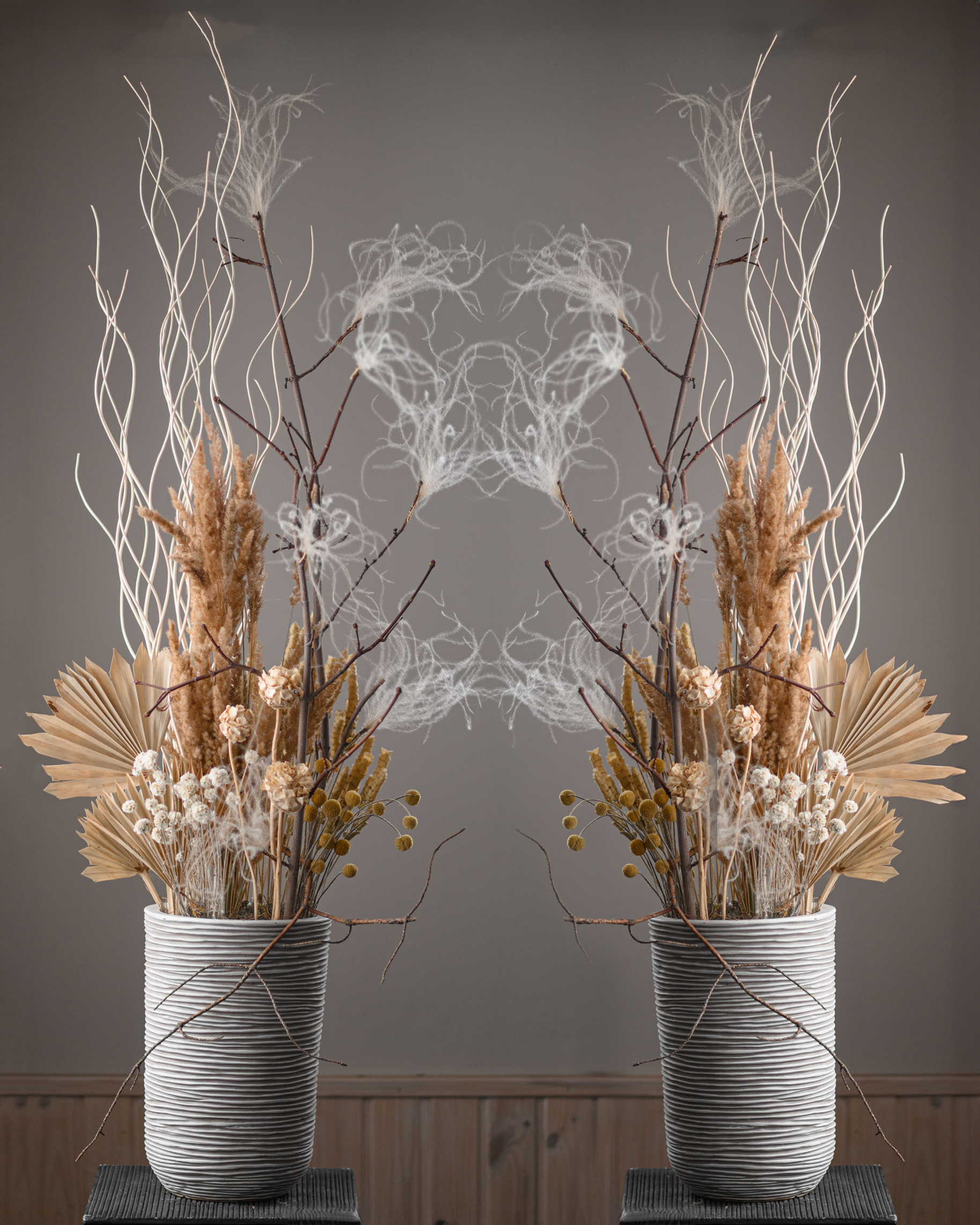 Two tall dried floral compositions with branching stems in textured pale vessels