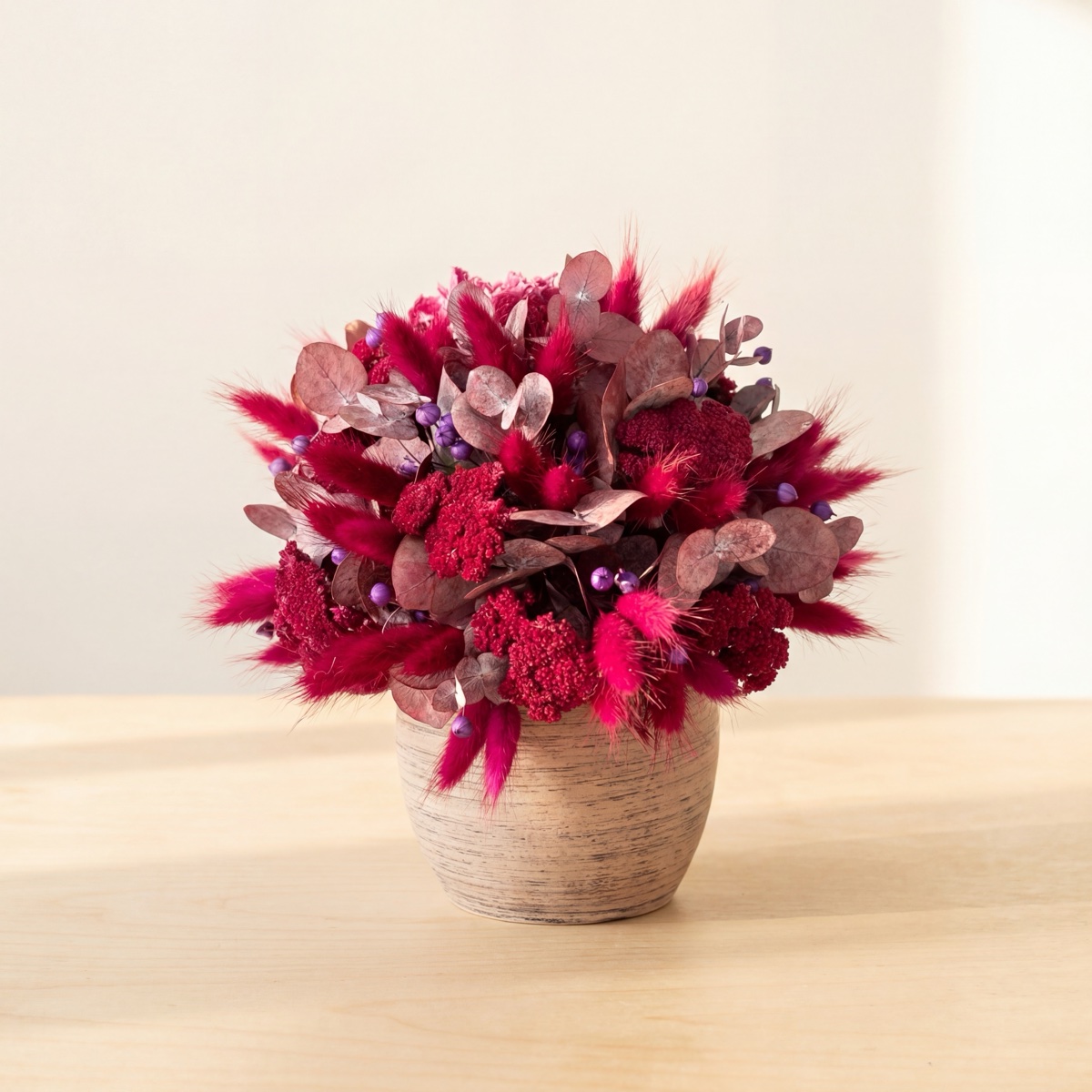 Rounded pink and burgundy dried flower arrangement in a light-coloured vessel